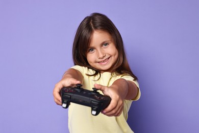 Photo of Happy little girl playing video game with controller on violet background