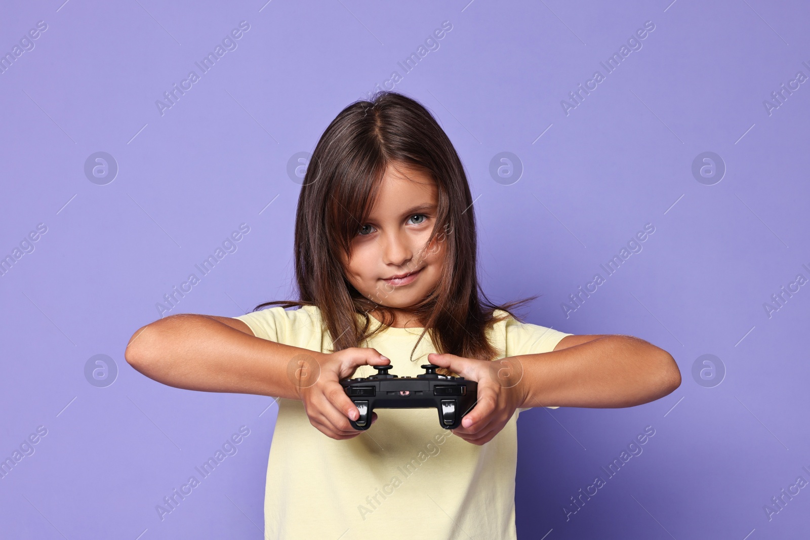 Photo of Cute little girl playing video game with controller on violet background