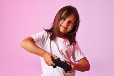 Photo of Cute little girl playing video game with controller on pink background