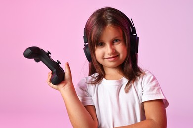 Photo of Cute little girl in headphones with controller on pink background