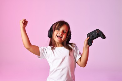 Photo of Happy little girl in headphones with controller on pink background