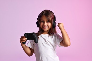 Photo of Happy little girl in headphones with controller on pink background