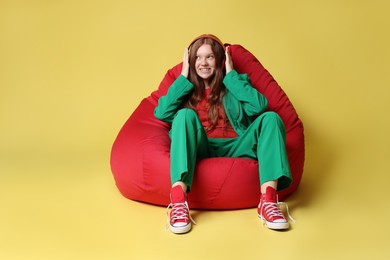 Photo of Teenage red-haired girl with headphones sitting on beanbag against golden background