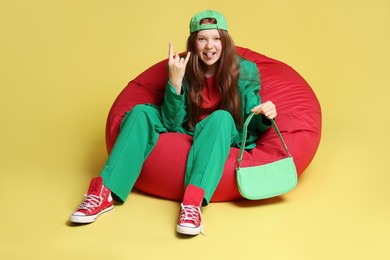 Photo of Teenage red-haired girl with bag sitting on beanbag against golden background