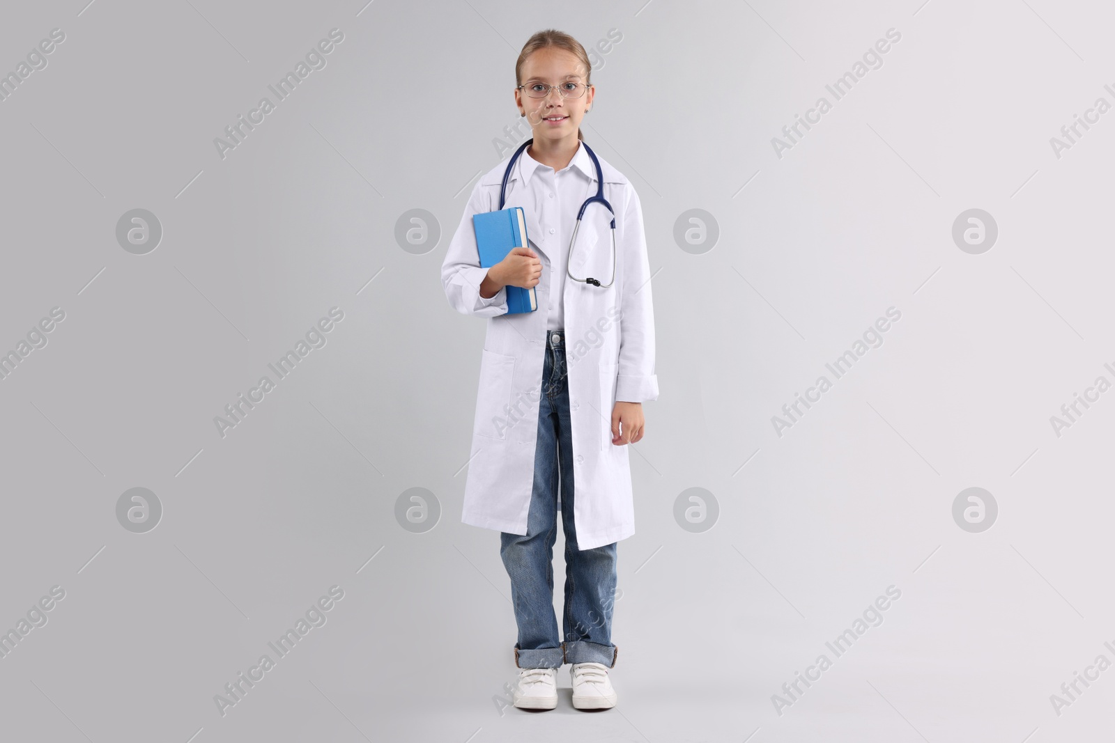 Photo of Girl with stethoscope and book pretending to be doctor on light grey background. Dreaming of future profession