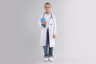 Photo of Girl with stethoscope and book pretending to be doctor on light grey background. Dreaming of future profession