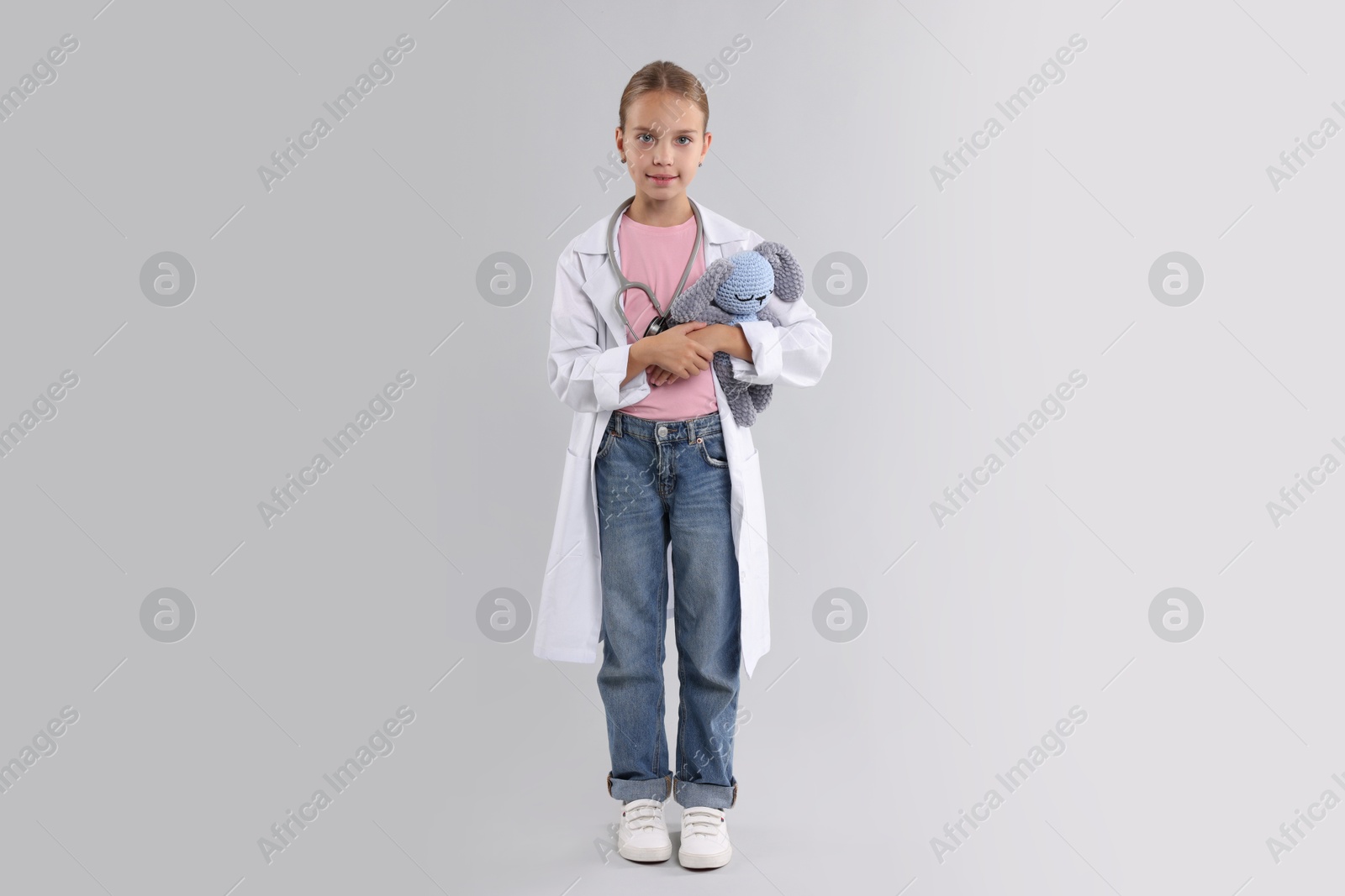 Photo of Girl with stethoscope and toy pretending to be doctor on light grey background. Dreaming of future profession