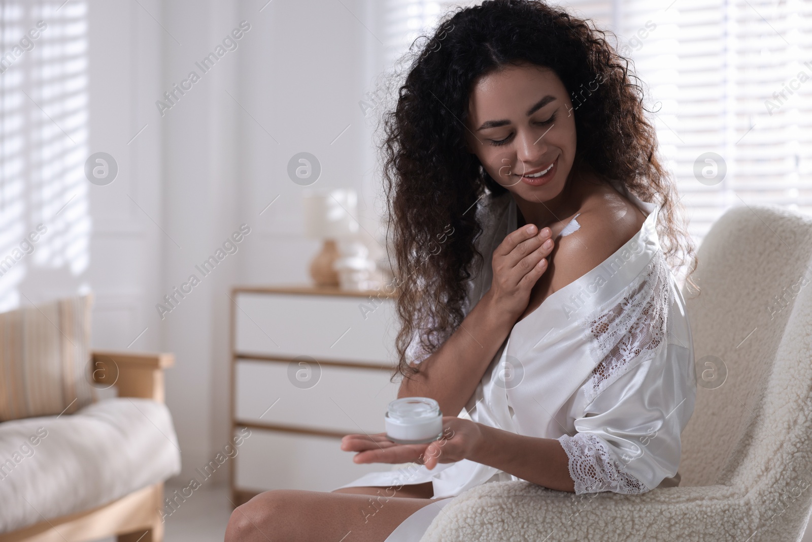 Photo of Young woman applying cream onto shoulder at home. Space for text