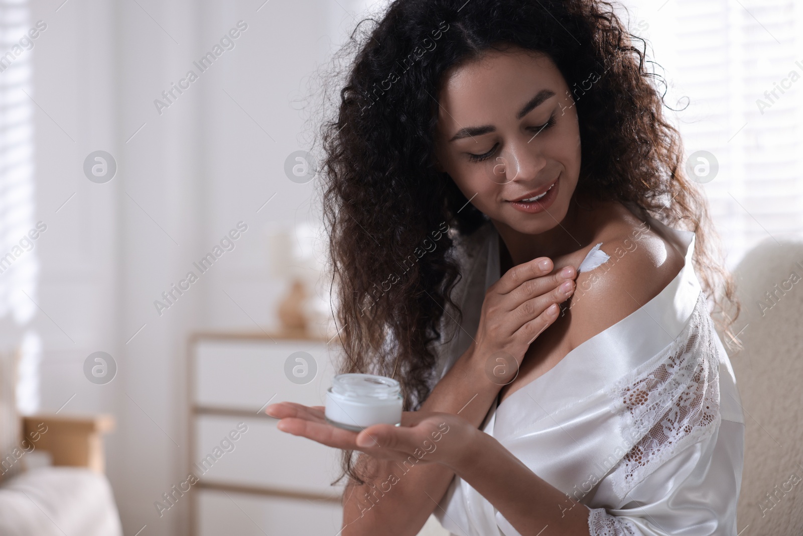 Photo of Young woman applying cream onto shoulder at home. Space for text