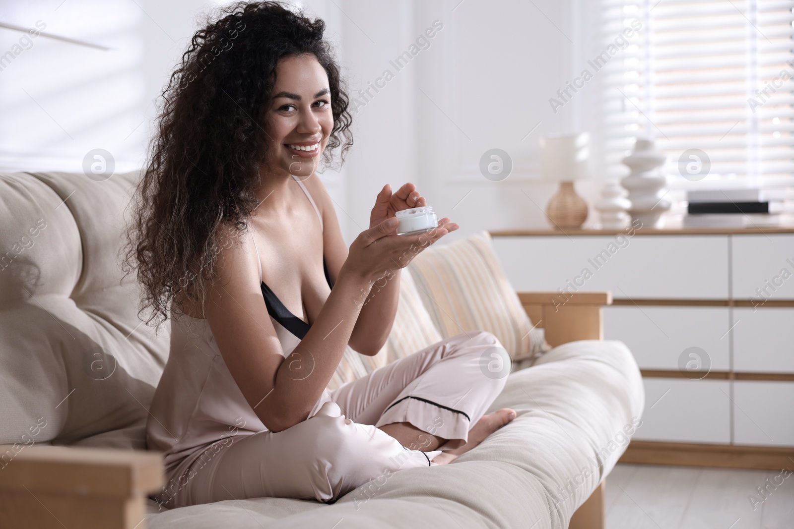 Photo of Young woman with jar of cream on sofa at home. Space for text