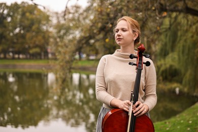 Photo of Beautiful young woman with cello in park, space for text