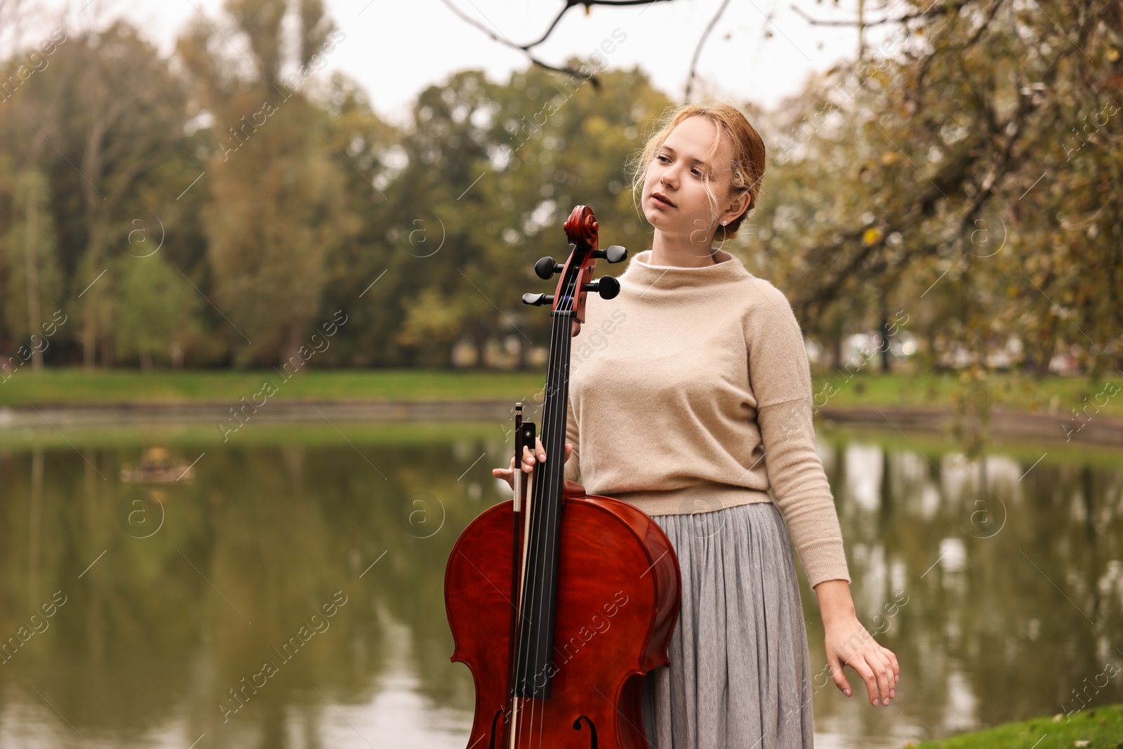 Photo of Beautiful young woman with cello in park, space for text