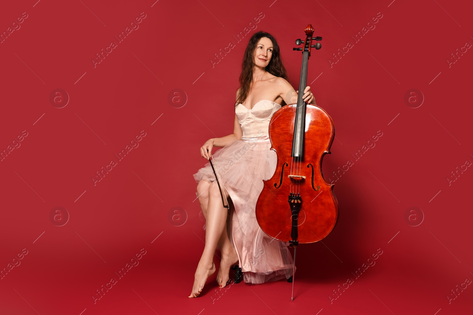 Photo of Beautiful woman with cello on red background