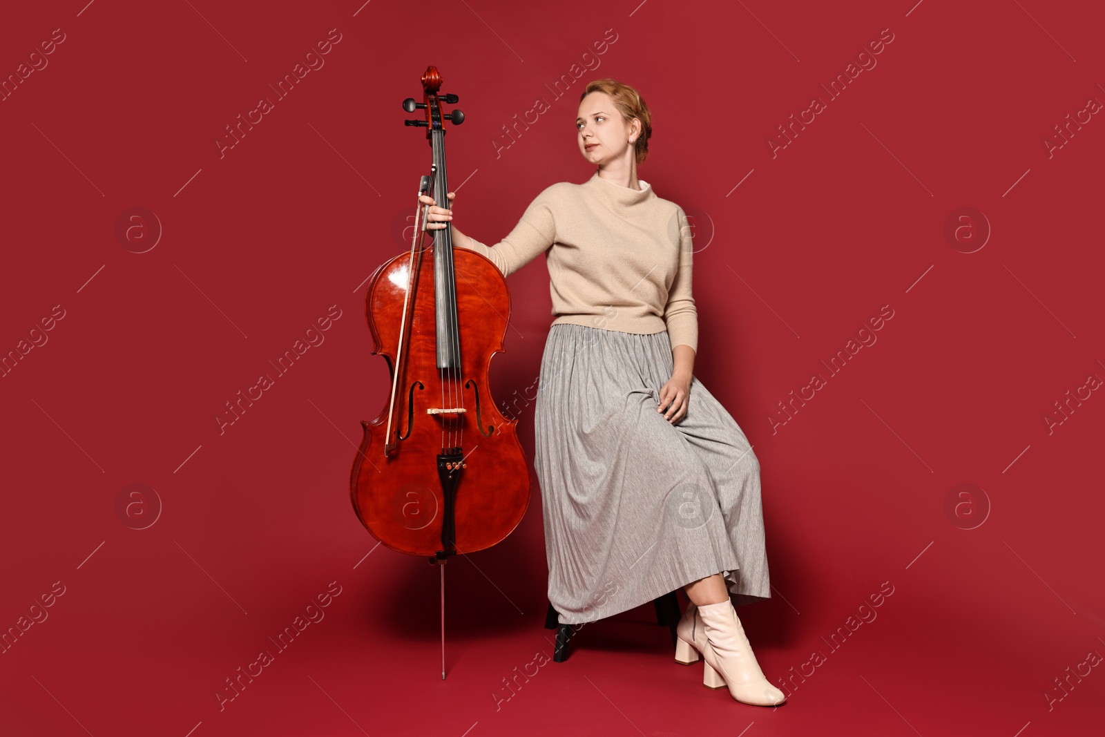 Photo of Beautiful young woman with cello on red background