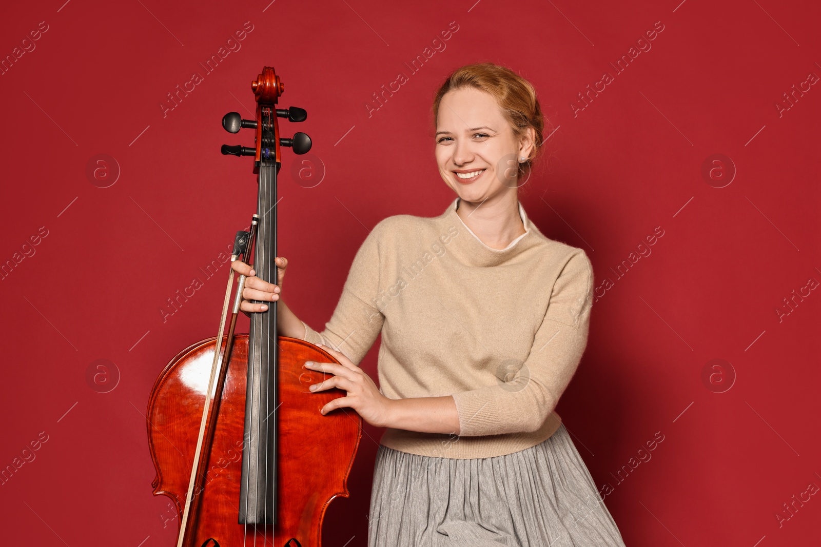 Photo of Beautiful young woman with cello on red background