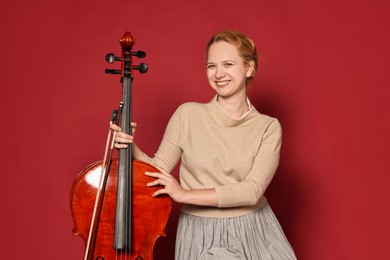 Photo of Beautiful young woman with cello on red background