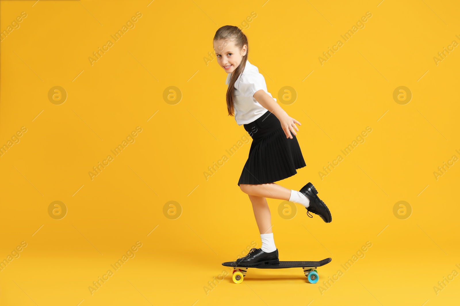 Photo of Little girl standing on penny board against yellow background