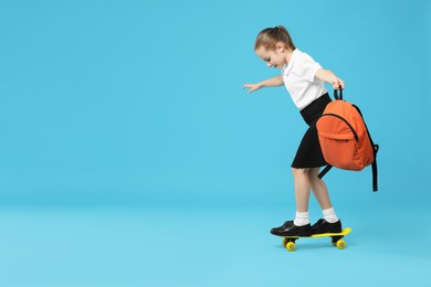 Photo of Little girl with backpack standing on penny board against light blue background, space for text