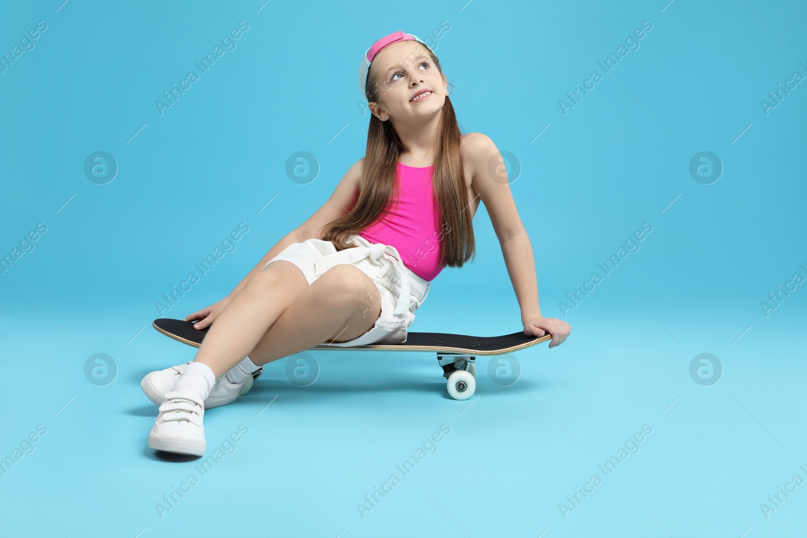 Photo of Stylish girl sitting on skateboard against light blue background