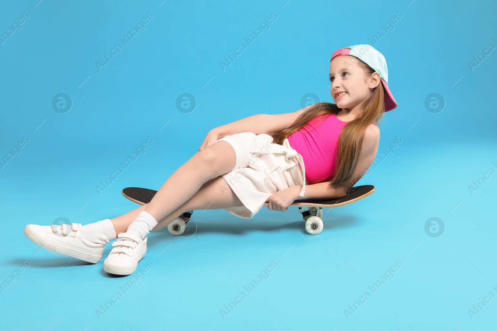 Photo of Stylish girl sitting on skateboard against light blue background