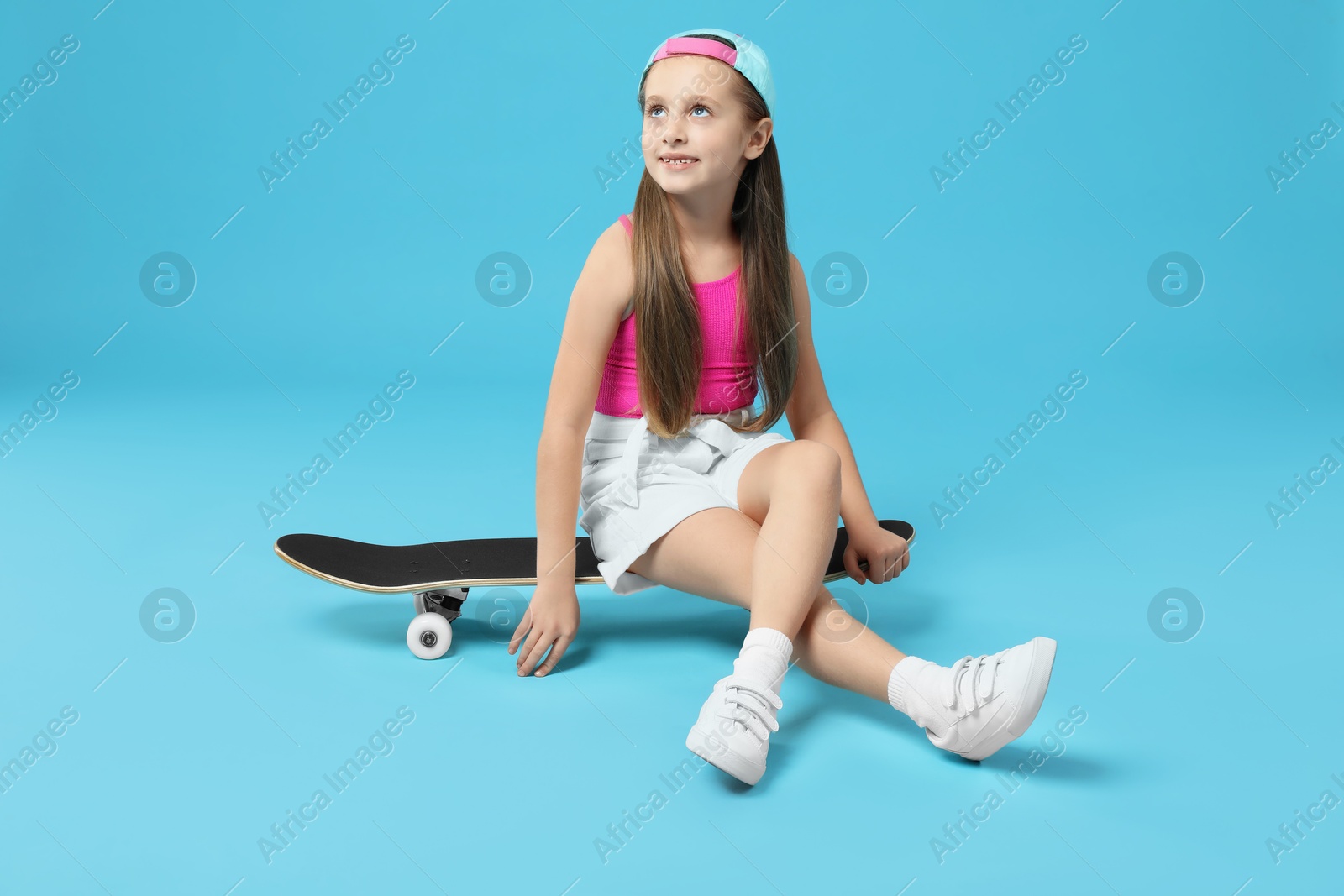 Photo of Stylish girl sitting on skateboard against light blue background