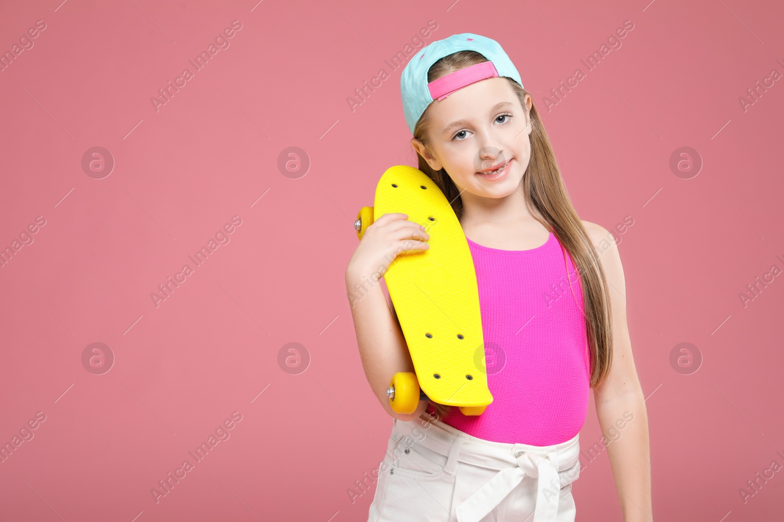 Photo of Little girl with penny board on pink background, space for text