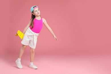 Photo of Little girl with penny board on pink background, space for text