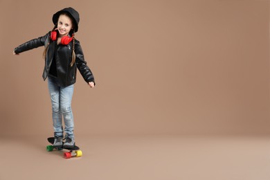 Photo of Little girl standing on penny board against pale brown background, space for text