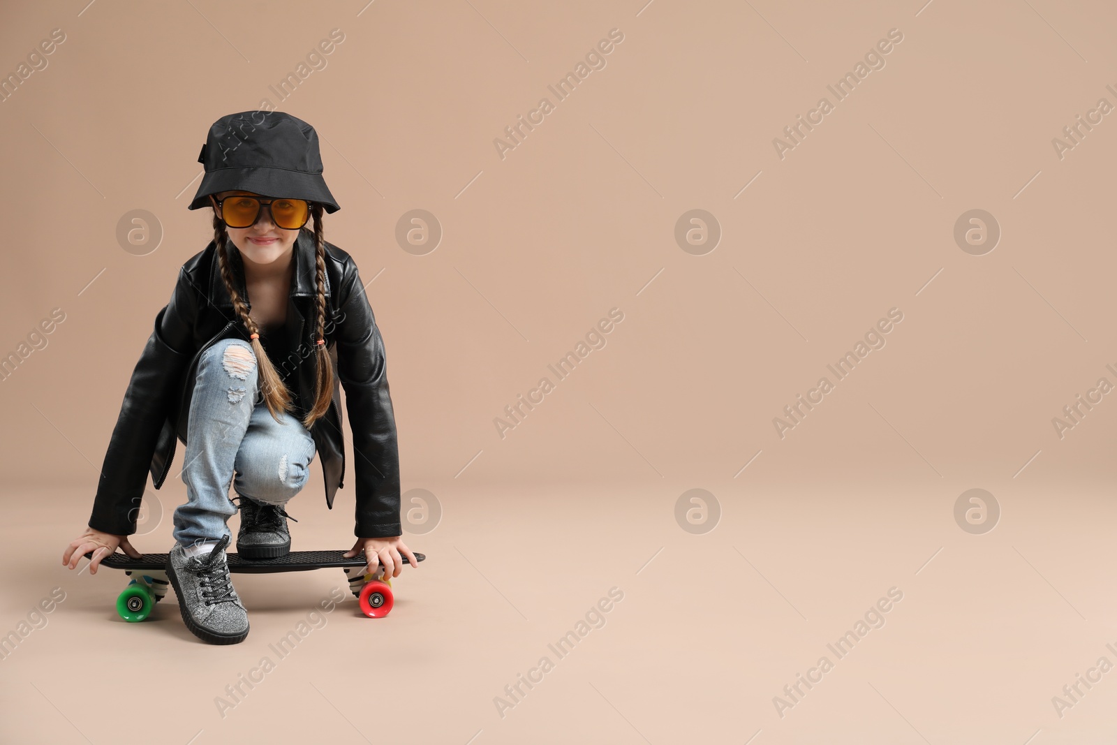 Photo of Little girl with penny board on pale brown background. Space for text