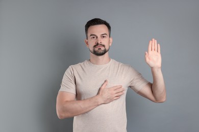 Photo of Man making promise with raised hand on grey background. Oath gesture