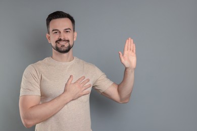 Photo of Man making promise with raised hand on grey background, space for text. Oath gesture