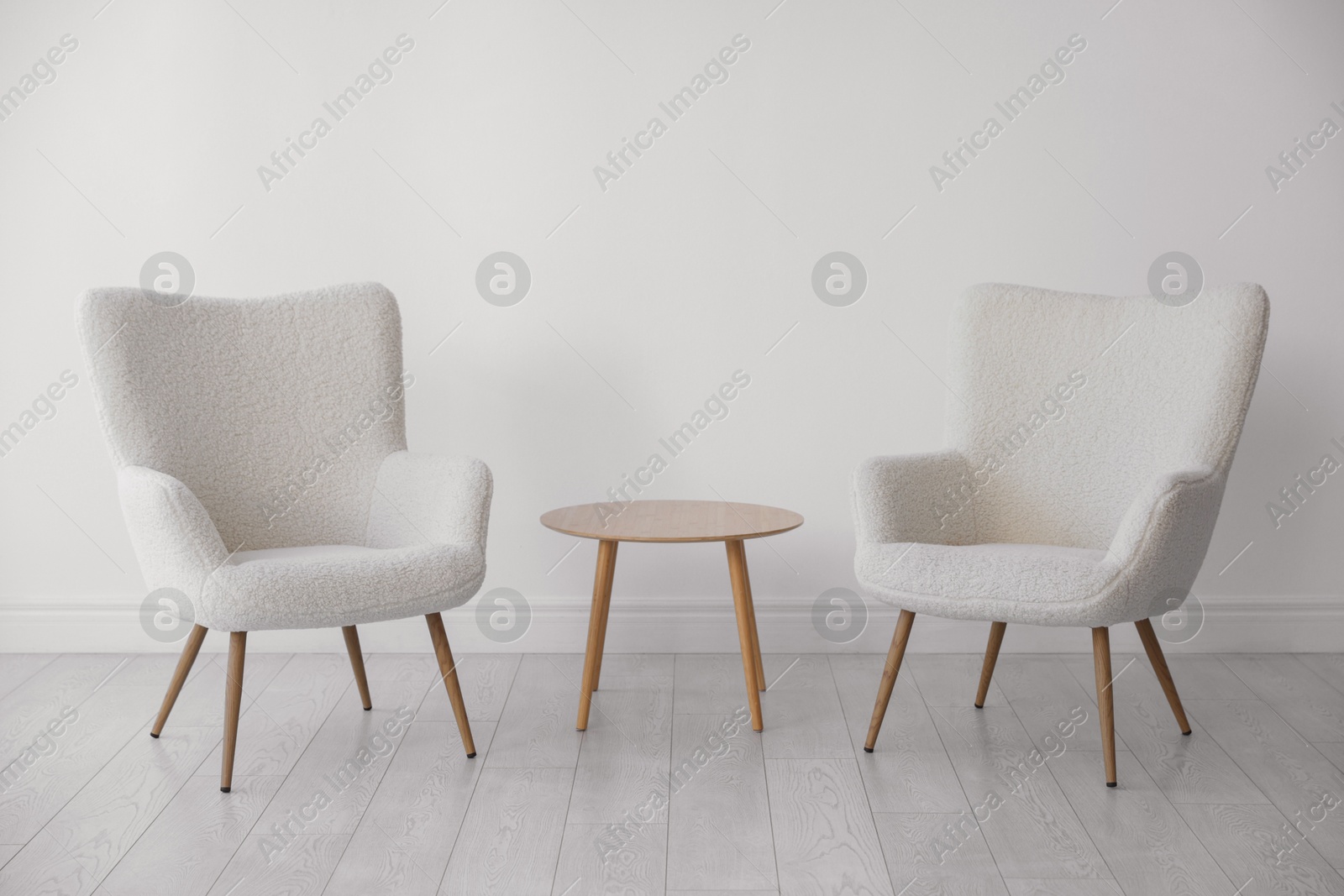 Photo of Soft armchairs and coffee table near white wall indoors