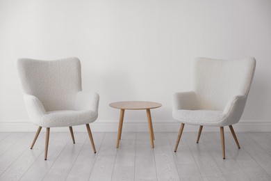 Soft armchairs and coffee table near white wall indoors