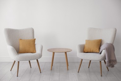 Photo of Soft armchairs and coffee table near white wall indoors