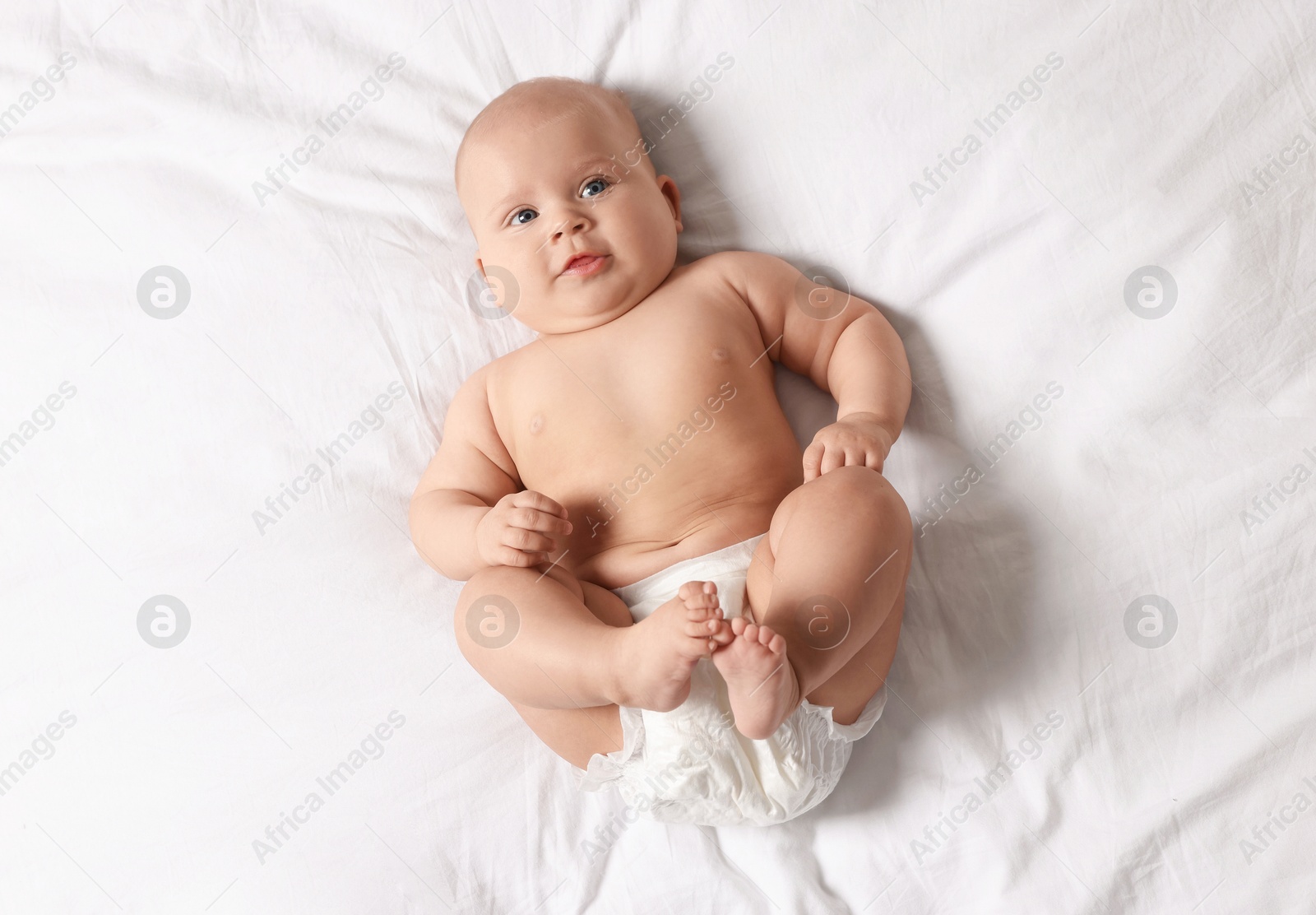 Photo of Cute little baby in diaper on bed, top view