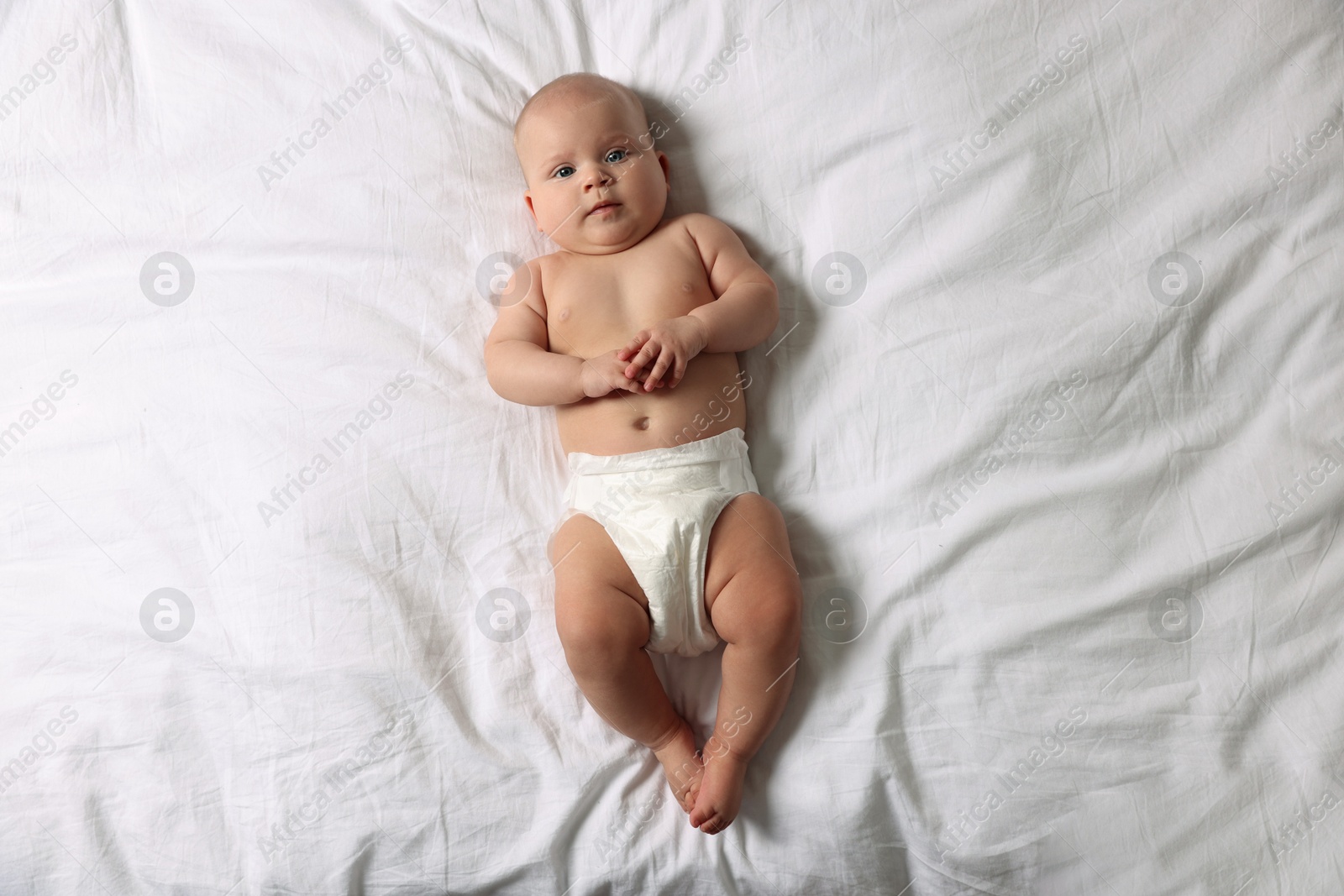 Photo of Cute little baby in diaper on bed, top view