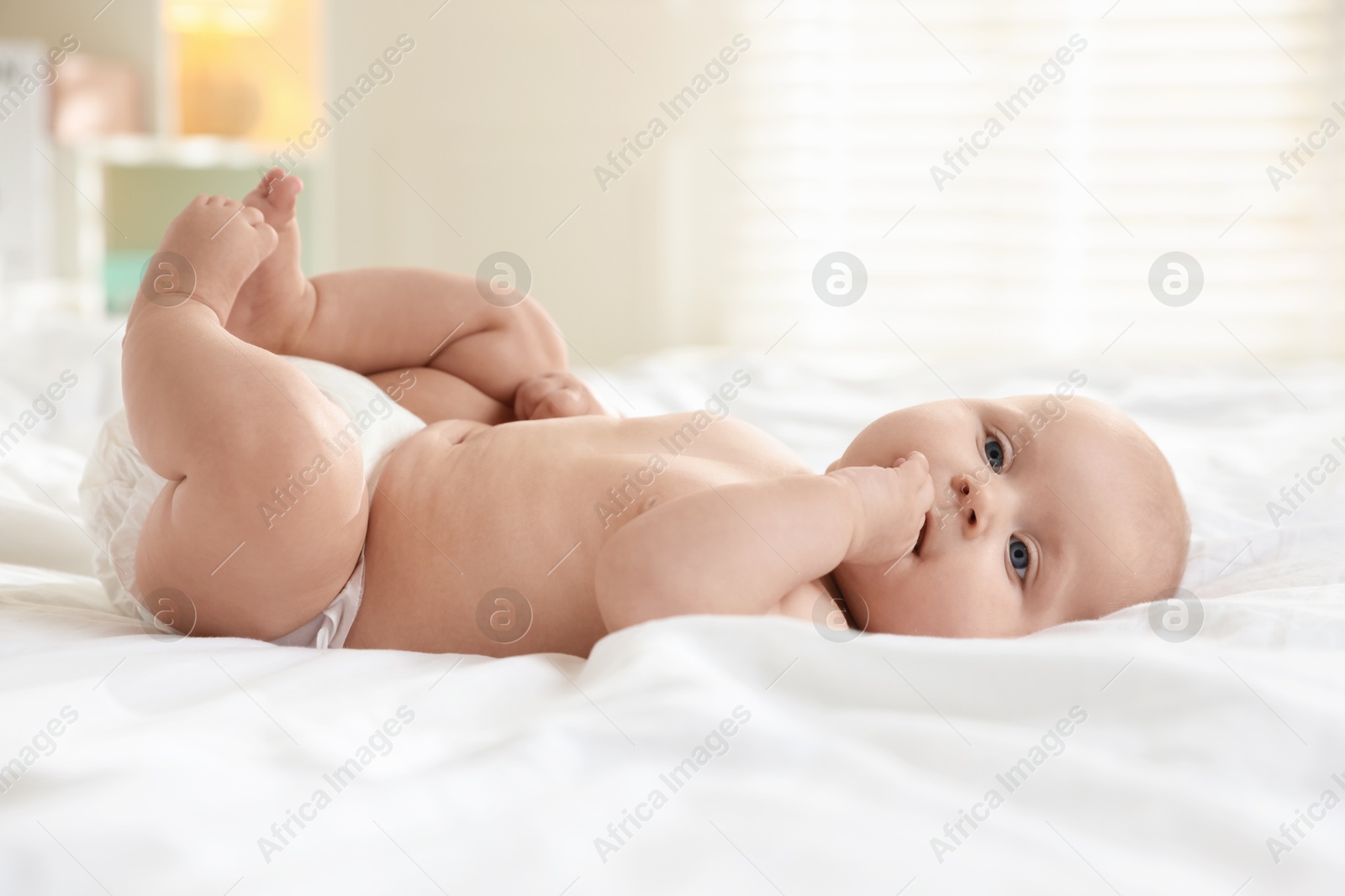 Photo of Cute little baby in diaper on bed indoors