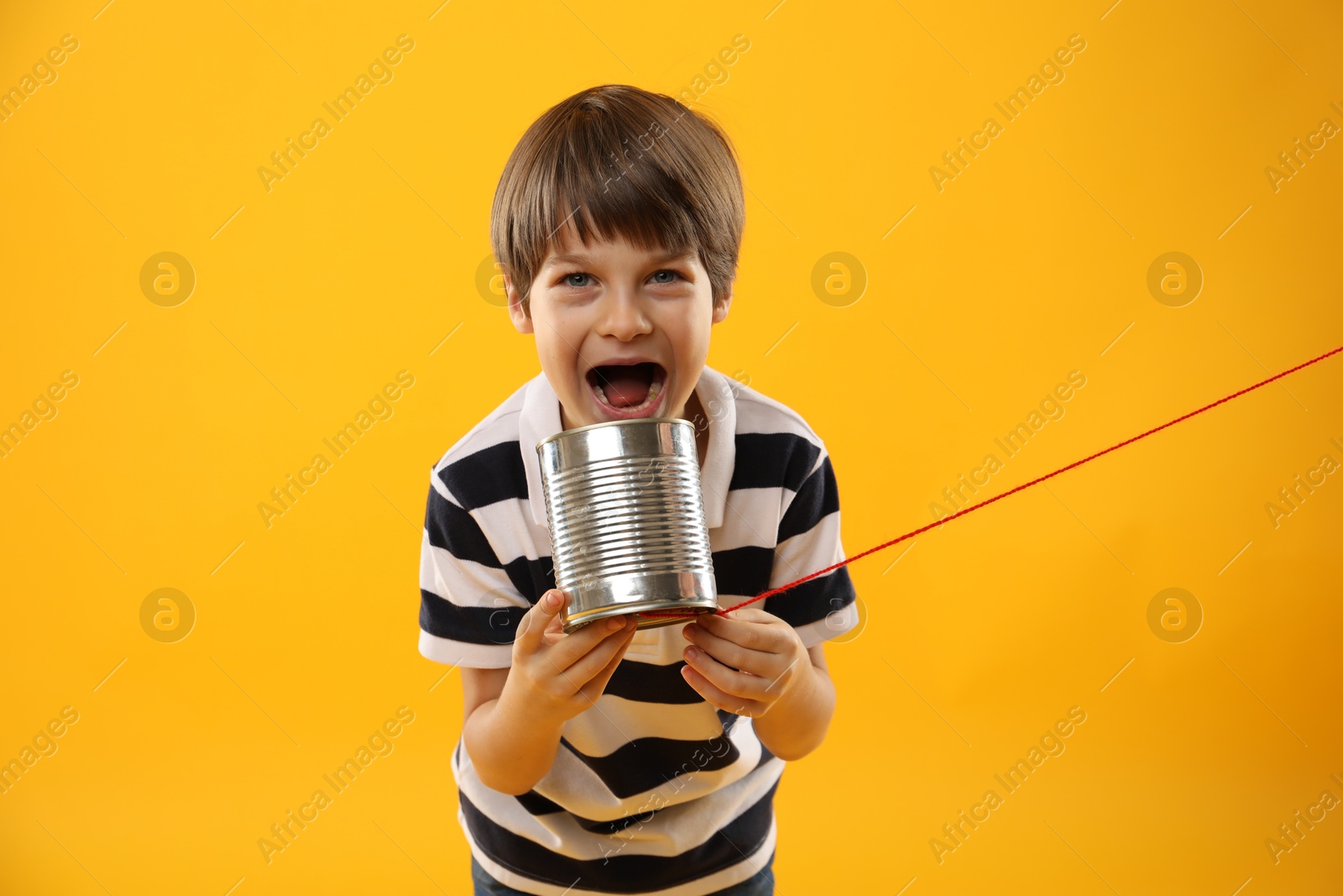 Photo of Boy using tin can telephone on yellow background