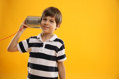 Photo of Boy using tin can telephone on yellow background, space for text