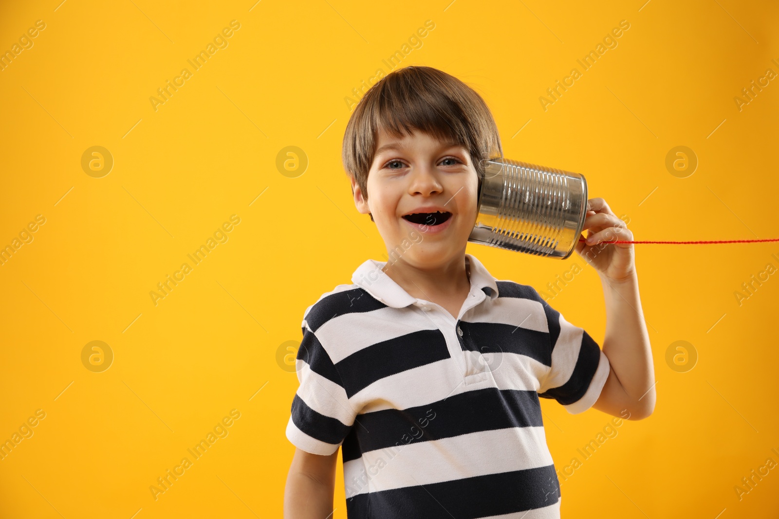 Photo of Boy using tin can telephone on yellow background, space for text