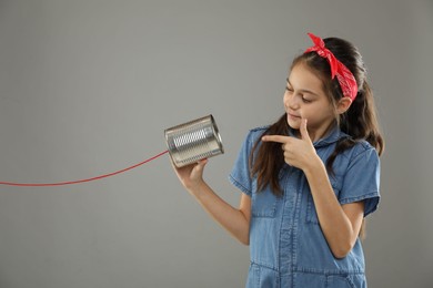 Photo of Girl pointing at tin can telephone on gray background