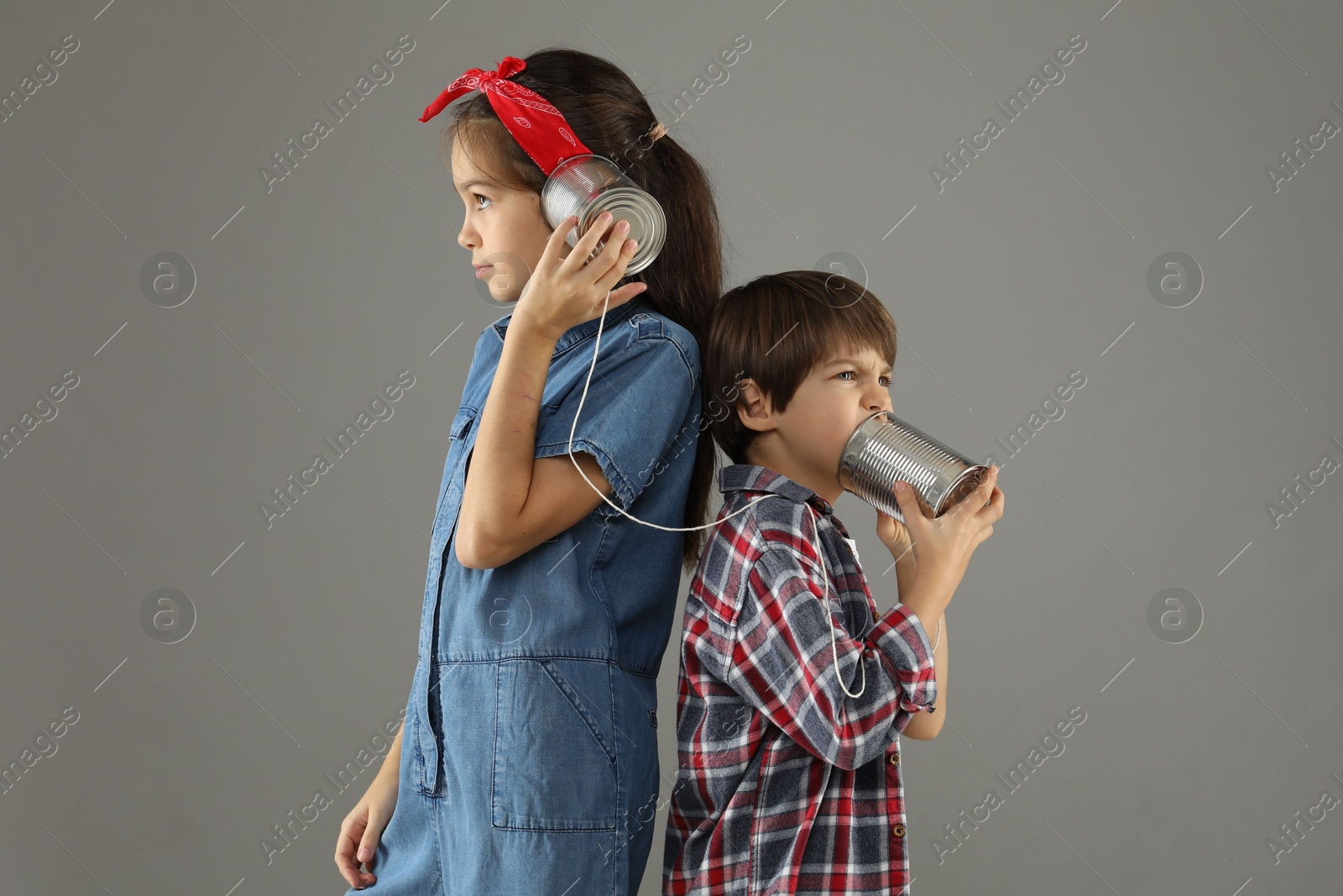 Photo of Girl and boy talking on tin can telephone against gray background