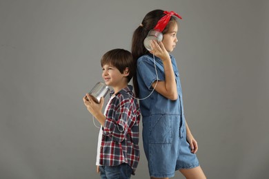 Photo of Girl and boy talking on tin can telephone against gray background