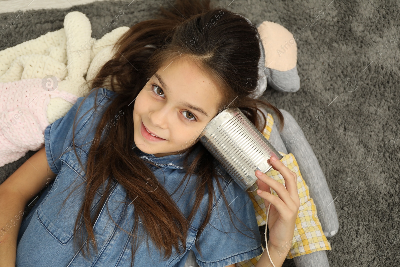 Photo of Girl using tin can telephone on gray rug, top view