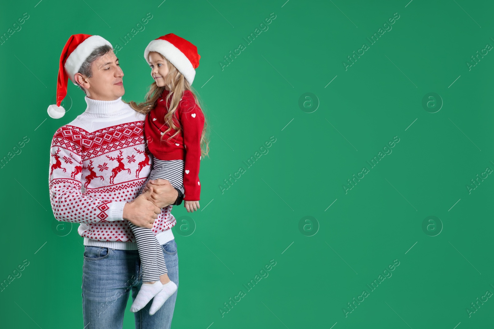 Photo of Father and daughter in Santa hats on green background, space for text. Christmas celebration