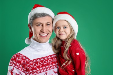 Photo of Father and daughter in Santa hats on green background. Christmas celebration