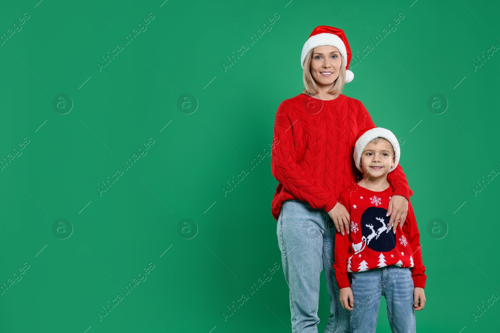 Photo of Mother and son in Santa hats on green background, space for text. Christmas celebration