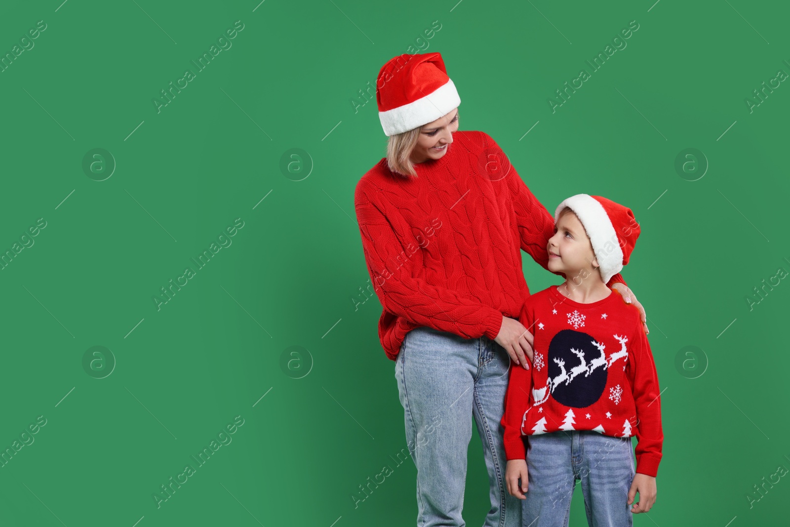 Photo of Mother and son in Santa hats on green background, space for text. Christmas celebration