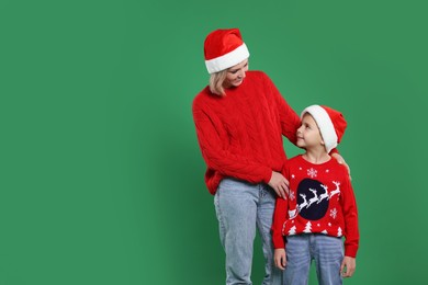 Photo of Mother and son in Santa hats on green background, space for text. Christmas celebration