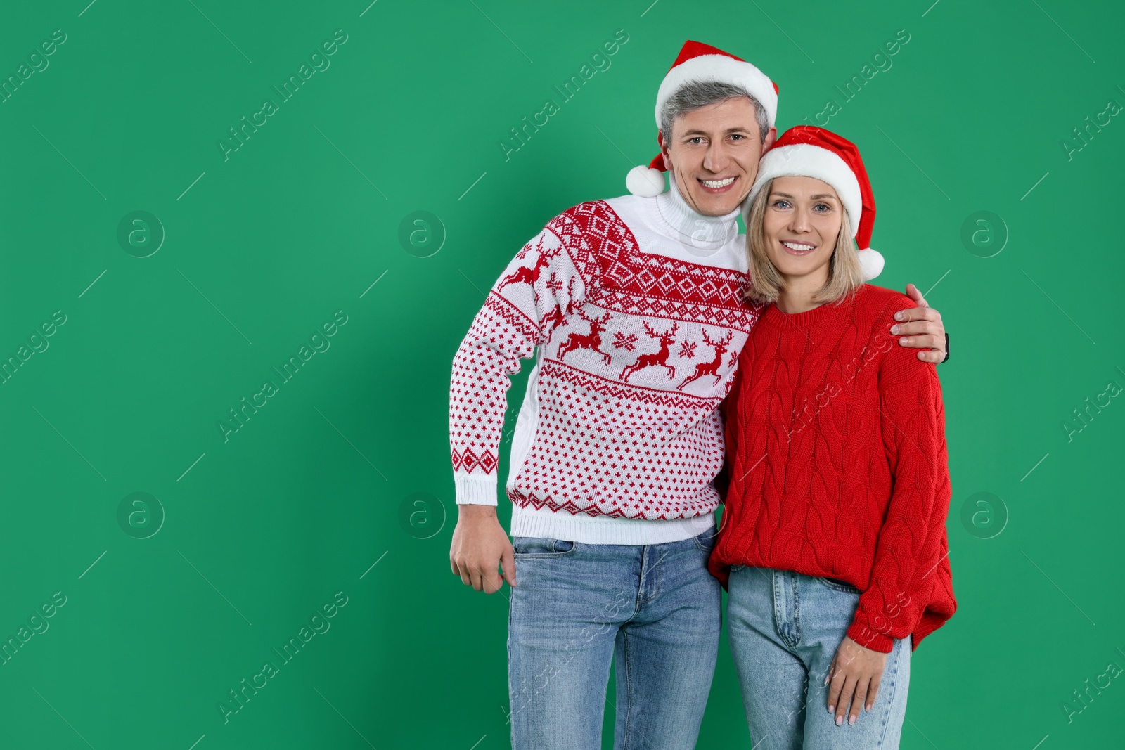 Photo of Happy couple in Christmas sweaters and Santa hats on green background. Space for text